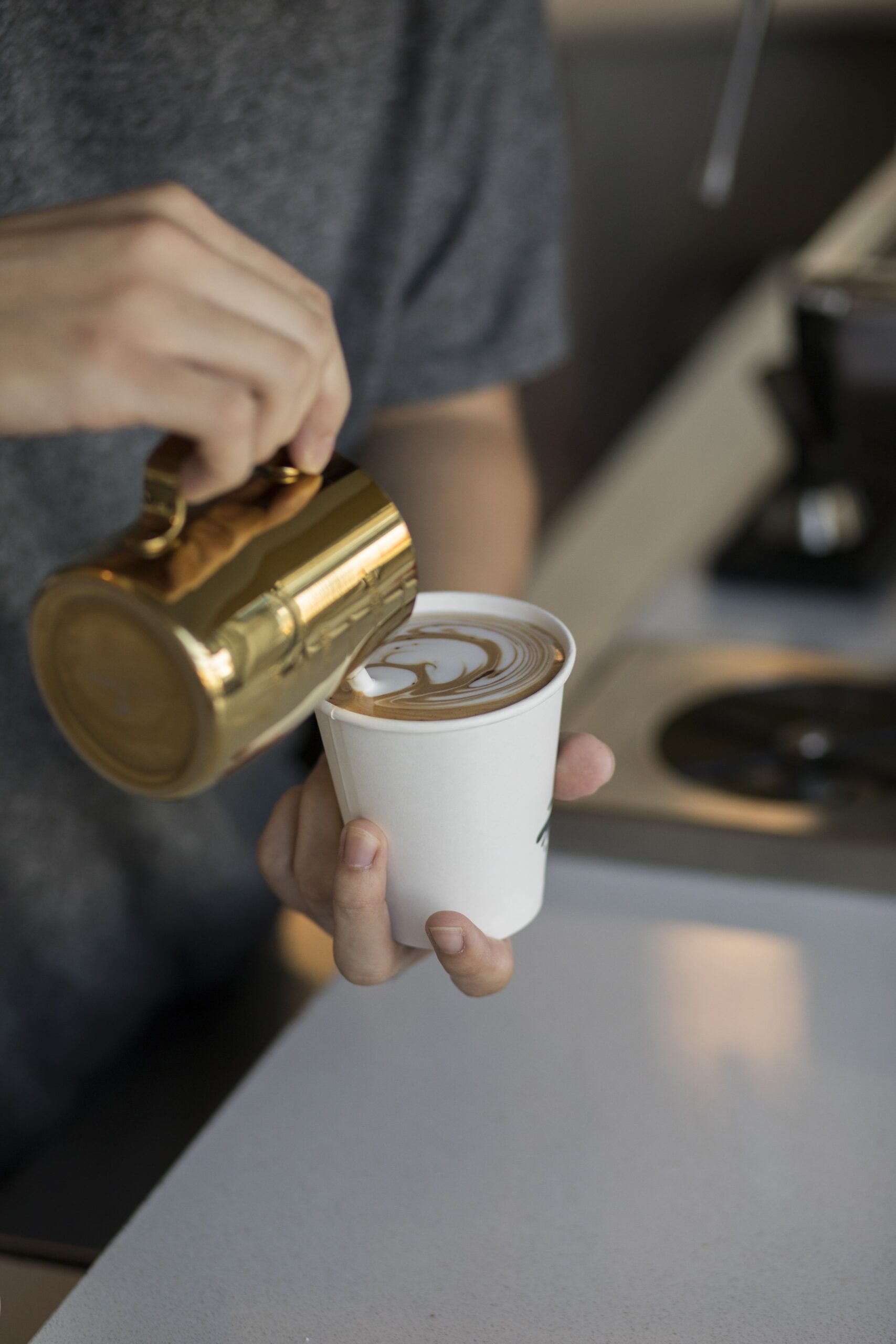 barista-pouring-cream-into-cappuccino-glass-making-beautiful-coffee-art